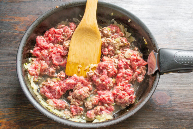 Breaking Up the Ground Beef While Cooking Using a spatula to break up ground beef as it cooks in a skillet.