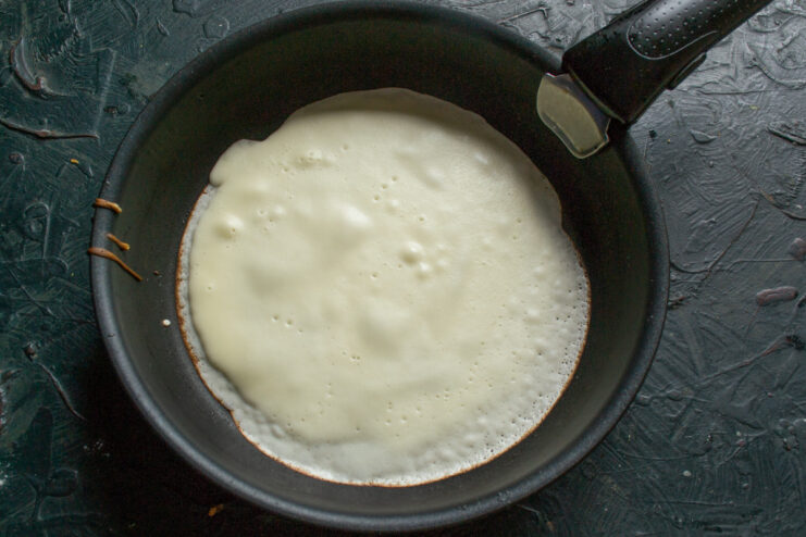 Frying the Thin Blinchiki Crepes to a Golden Brown A thin, golden-brown blin (crepe) cooking in a hot skillet.