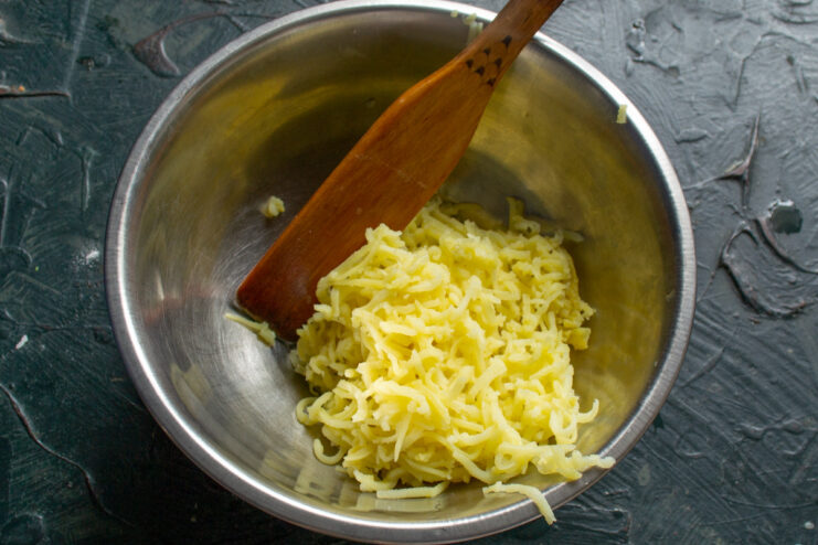 Preparing the Potato Filling: Grating Boiled Potatoes Grating a potato boiled in its skin to create a smooth filling.