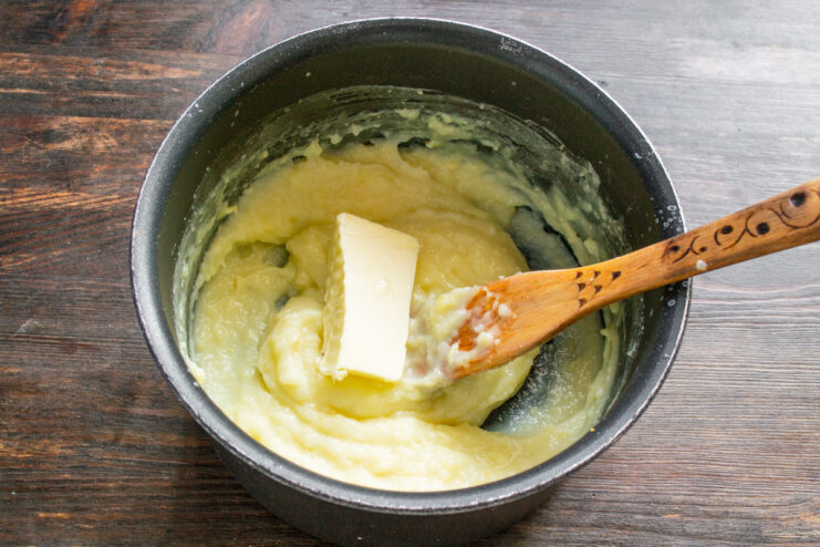 Adding a pat of softened butter to the cooled lemon custard in a saucepan.