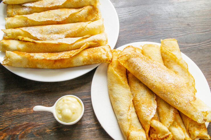 Sifting powdered sugar over a plate of rolled, custard-filled blinchiki.