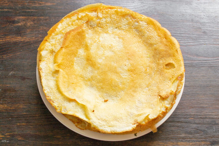 A neat stack of freshly cooked, thin golden pancakes on a plate.