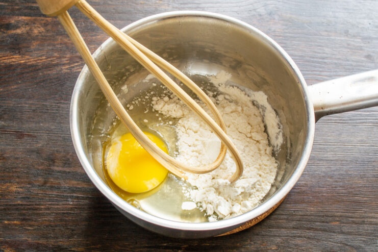 A cracked egg and a pile of flour in a white bowl, the first step for the custard.