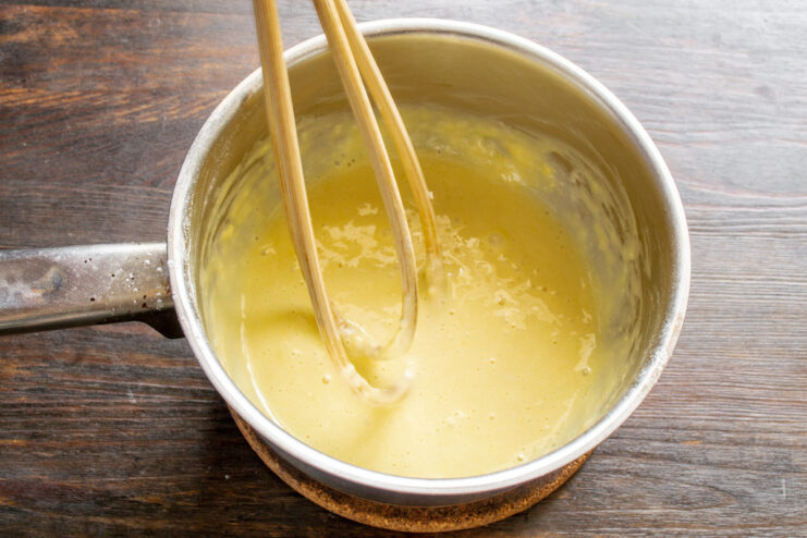 A whisk mixing egg and flour into a smooth, thick paste in a white bowl.