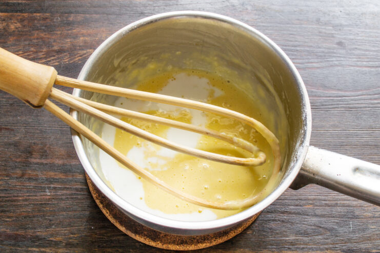 Pouring a small amount of milk into the egg and flour mixture in a bowl.