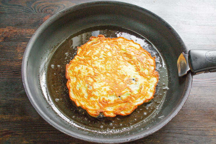 Flipping the Zucchini Pancake to Cook the Other Side A golden-brown zucchini pancake being flipped with a spatula in a skillet.
