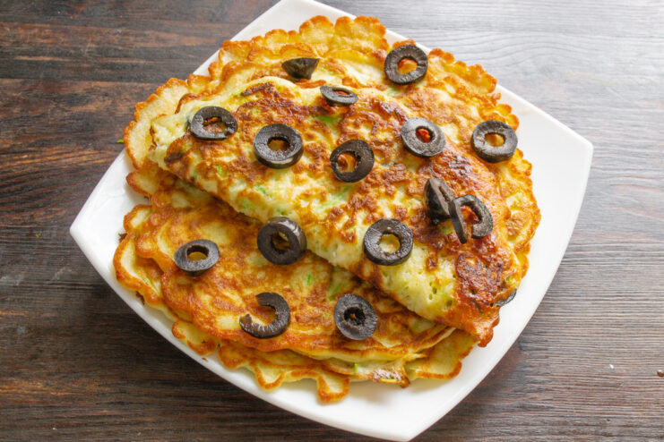 Serving Zucchini Pancakes with Pesto Sauce A stack of zucchini pancakes served on a plate with a side of pesto sauce.