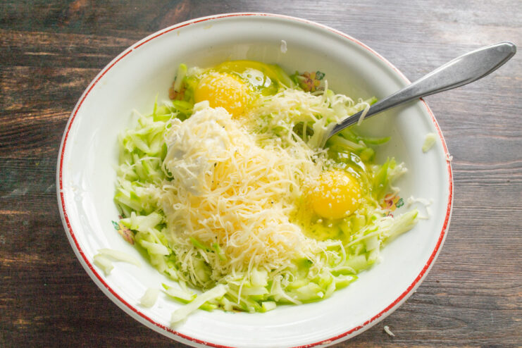 Adding Eggs and Salt to the Pancake Batter Two eggs cracked into the zucchini and cheese mixture in a bowl.