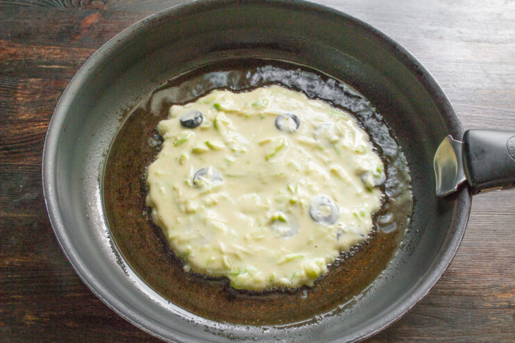 Frying the Zucchini Pancakes Spoonfuls of zucchini pancake batter being poured into a hot skillet to fry.