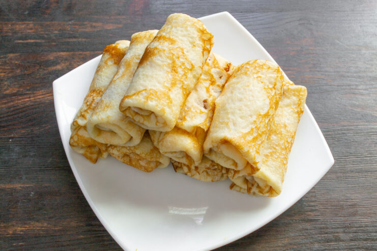 A Batch of Freshly Made, Rolled Bliny A plate with a stack of about ten thin bliny, rolled and filled.