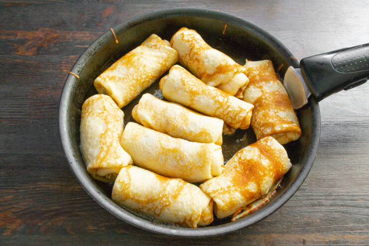 Pan-Frying the Filled Bliny Until Golden Filled bliny rolls being fried in a skillet with butter until they are golden brown and crispy.