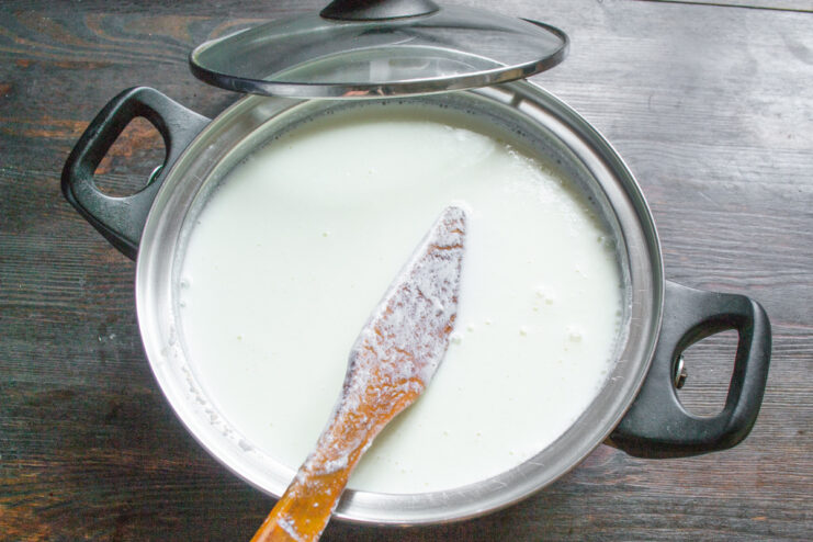 Starting the Tvorog: Combining Hot Milk and Kefir Kefir being poured into a pot of warm milk to begin the process of making homemade tvorog.