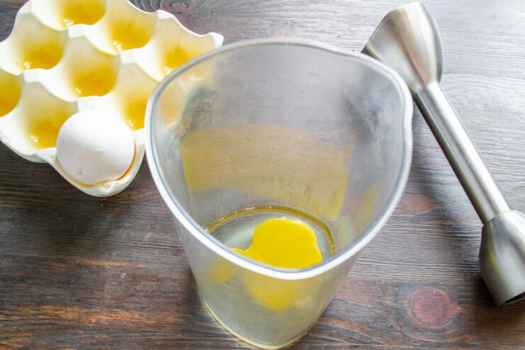 Preparing the Bliny Batter: Starting with an Egg A single raw egg cracked into a tall transparent cup for an immersion blender.