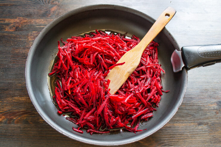 Step-by-step: Making the flavorful beet and tomato base for borscht Grated beets being added to a frying pan to start the borscht base.