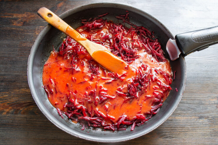 Adding tomato juice to the beets for a tangy borscht base Pouring tomato juice into the pan with sautéed beets.