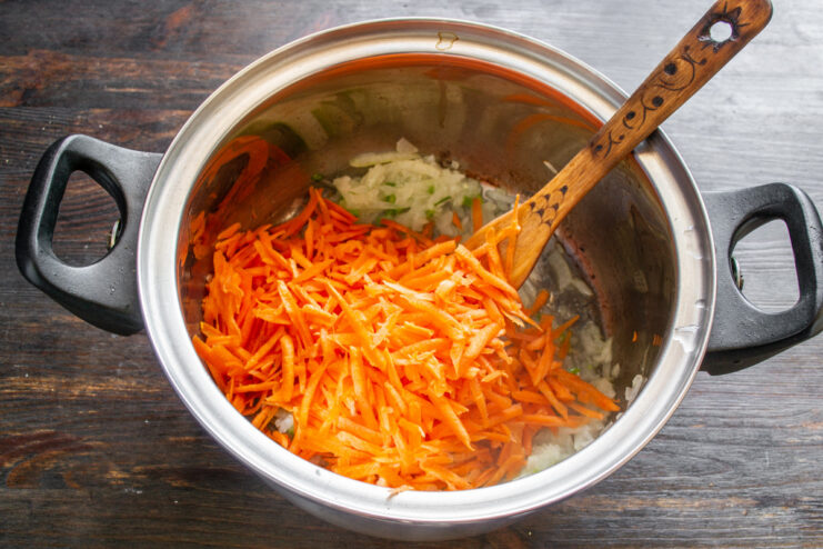 Grating fresh carrots to add sweetness to the borscht A hand grating a carrot on a coarse box grater.