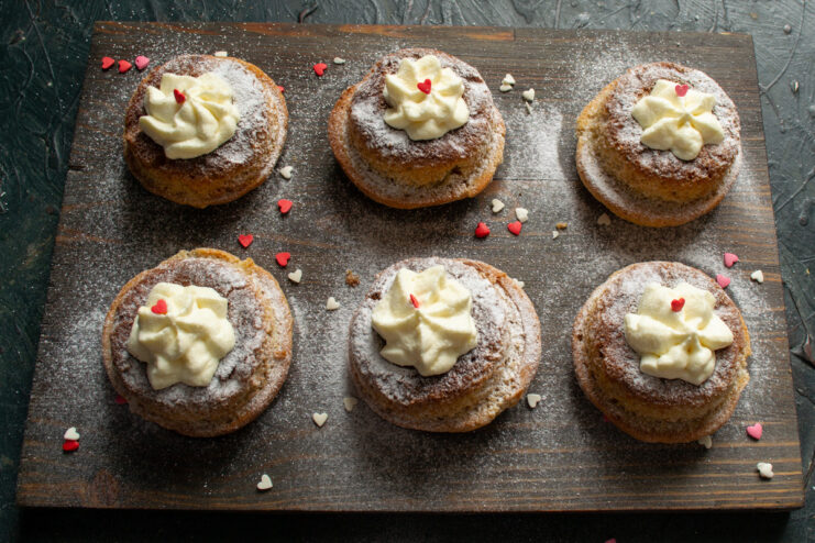 The final touch: dusting the buns with powdered sugar before serving. Finished apple and cream buns on a plate, being dusted with powdered sugar, next to a cup of coffee.