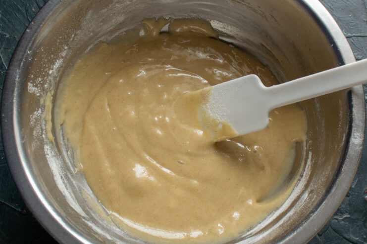 Mixing the batter until just combined for tender and fluffy buns. A smooth, lump-free batter for apple buns in a glass bowl with a whisk.