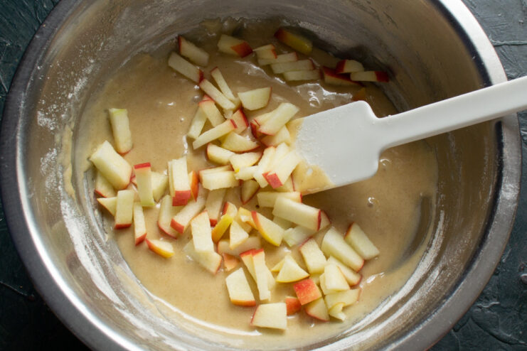 Preparing the apples: dicing them finely to add to the batter. A hand dicing a fresh apple into small cubes on a cutting board.