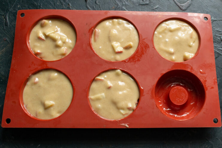 Filling the donut mold with apple batter before baking. A silicone donut mold being filled with apple bun batter using a spoon.