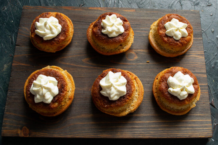 Filling the cooled apple buns with freshly whipped cream using a piping bag. A hand using a piping bag to fill the center of a baked apple bun with whipped cream.