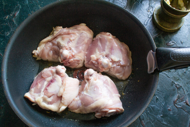 Chicken pieces being seared skin-side down in a hot black skillet.