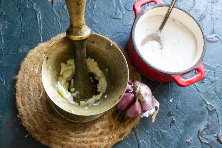 Smashed garlic cloves being ground with salt in a stone mortar.