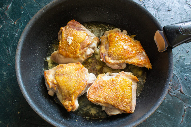 White wine being poured into a skillet with seared chicken and spices.