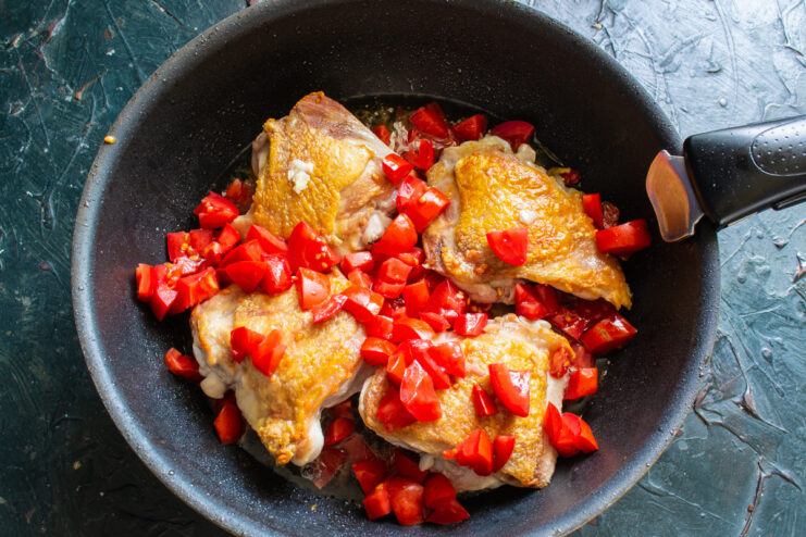 Diced red tomatoes being added to the skillet with chicken.
