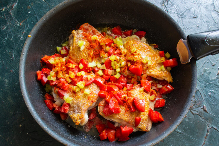 Diced bell peppers being added to the chicken and tomato mixture in the skillet.