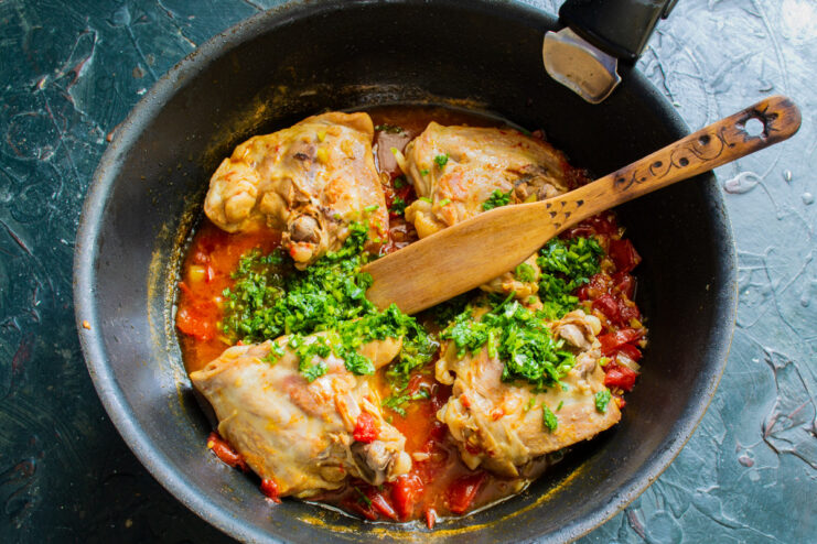 Chopped fresh cilantro being added to the finished Chakhokhbili in the skillet.