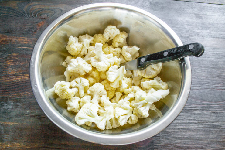 Step 1: Preparing the cauliflower for marinating A head of cauliflower being broken into small florets on a wooden cutting board.