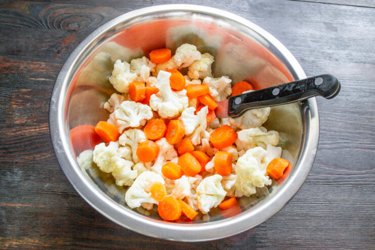 Step 2: Slicing carrots for the vegetable mix A peeled carrot being sliced into thin rounds on a cutting board.