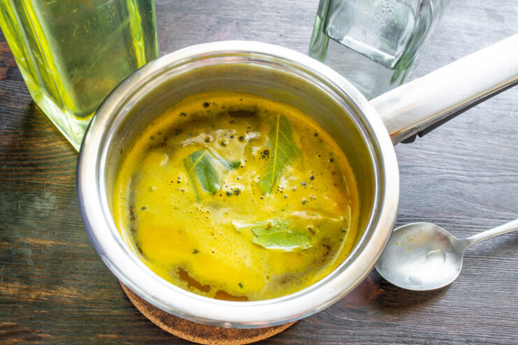 Step 7: Finishing the marinade with vinegar Pouring white wine vinegar from a bottle into the saucepan with the hot marinade liquid.