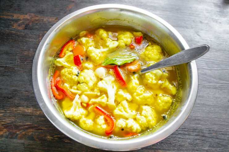 Step 8: Combining vegetables and marinade Hot, spiced marinade being poured from a saucepan over the blanched vegetables in a white bowl.