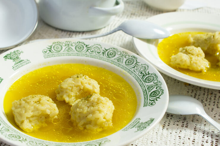 A bowl of clear chicken broth with several white rice dumplings, ready to be served.