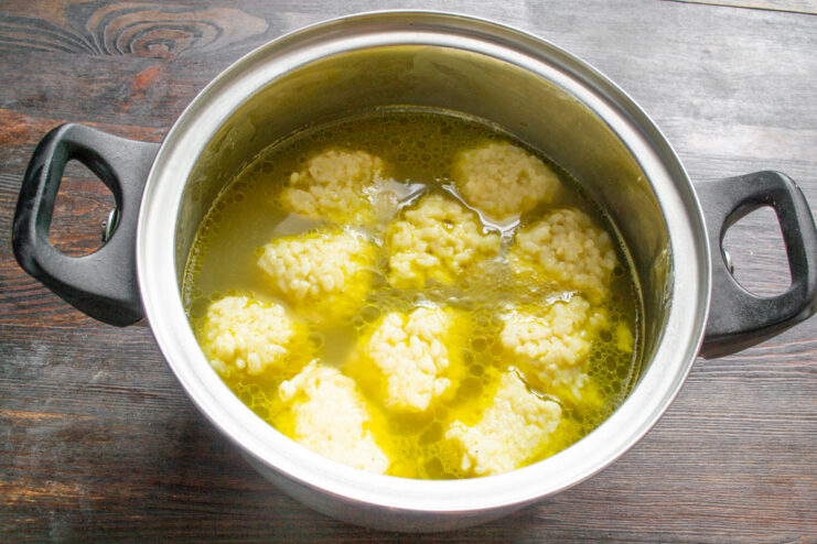 Cooking rice dumplings until they are perfectly done Rice dumplings floating in a pot of simmering chicken broth.