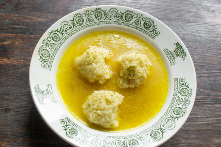 Serving the finished chicken broth with rice dumplings A ladle serving hot chicken broth with rice dumplings into a white bowl.