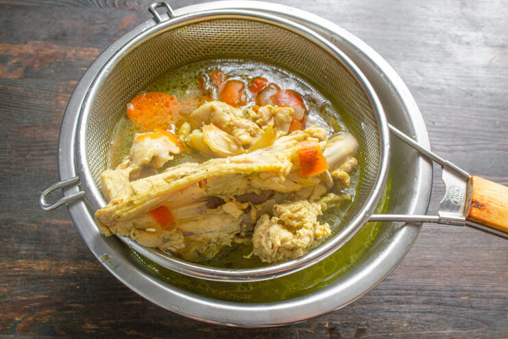 How to get a clear chicken broth by straining Straining golden chicken broth from a pot through a fine-mesh sieve into a bowl.