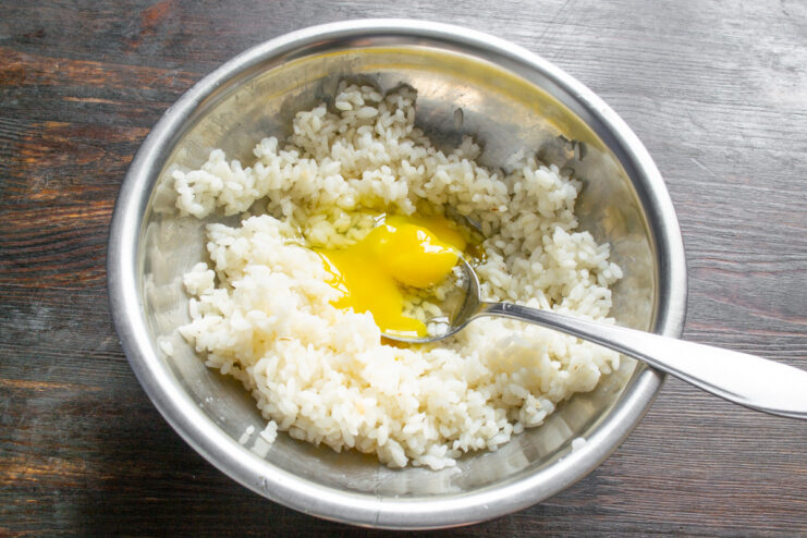 Binding the rice dumpling mixture with an egg A bowl of cooked rice with a cracked egg on top, ready to be mixed for dumplings.