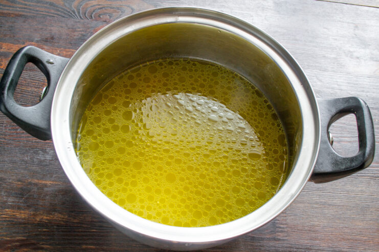 Heating the clear broth before adding dumplings Pouring clear, strained chicken broth back into a clean pot on the stove.