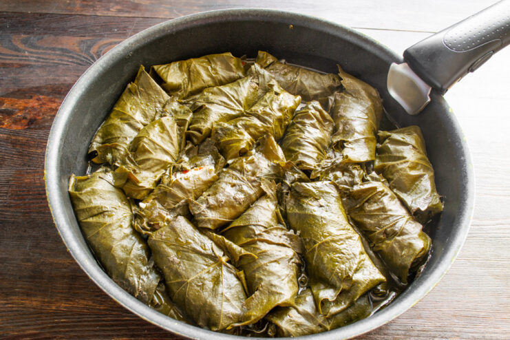 Preparing Dolma for simmering: adding water to the pot Hot water being poured into a pot of arranged Dolma, covering them completely.