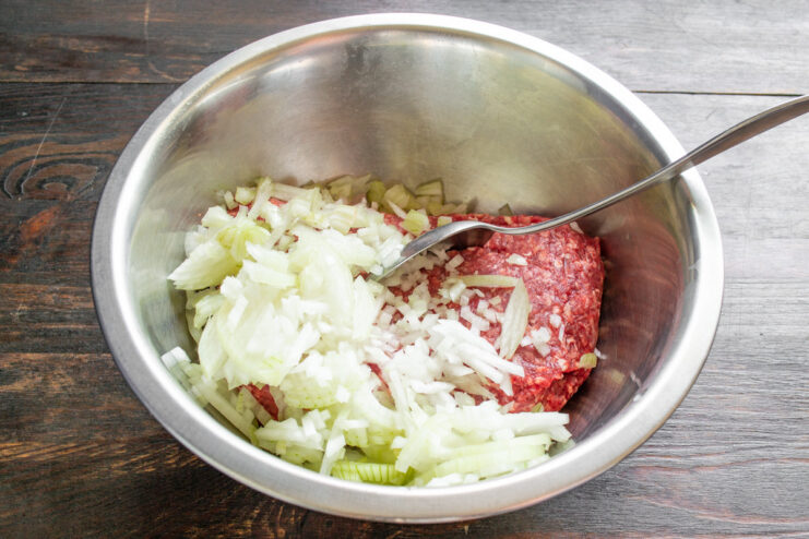 Preparing the filling for Dolma: adding onions to the meat A bowl of ground beef with finely diced onions being added to it.