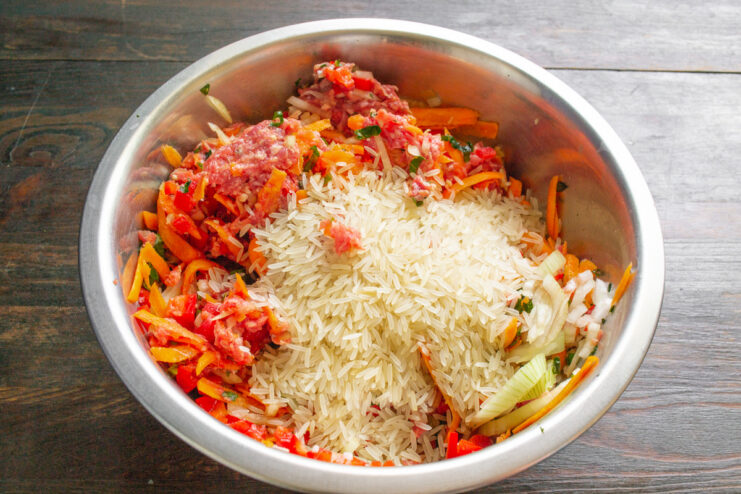 Adding rice to the Dolma meat and vegetable mixture Rinsed basmati rice being added to a bowl with minced meat and vegetables.