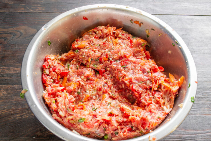 Mixing the savory filling for Dolma by hand Hands thoroughly mixing the minced meat, rice, and vegetable filling in a bowl.