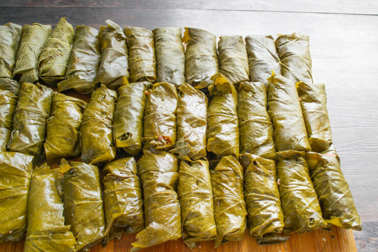 Step-by-step guide to rolling Dolma A grape leaf being tightly rolled around a portion of the meat filling on a wooden board.