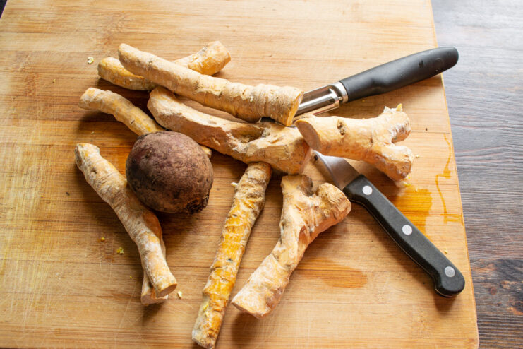 Fresh Ingredients for Horseradish Sauce: Horseradish Roots and a Beet Fresh horseradish roots and a whole raw beet on a wooden surface, ready for making the sauce.