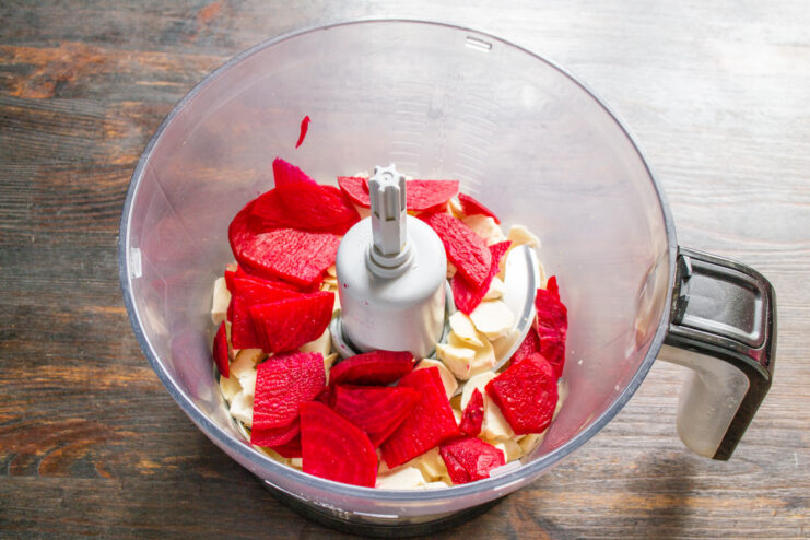 Adding Beetroot for that Vibrant Pink Color Thinly sliced raw beet being added to a blender bowl with chopped horseradish.