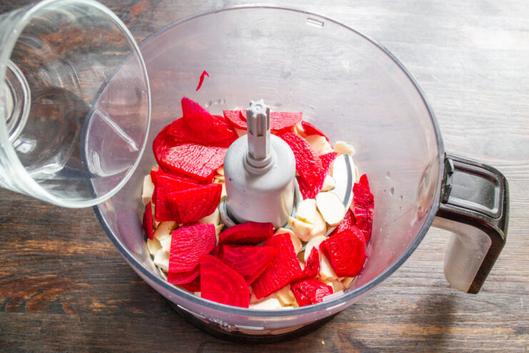 Adding Water to Help Blend the Horseradish and Beets Pouring cold filtered water into the blender bowl containing horseradish and beet slices.
