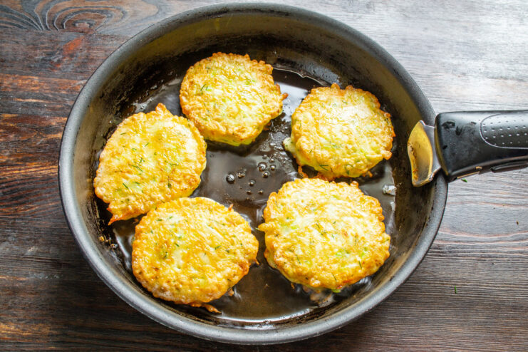 Frying Draniki to a Perfect Golden-Brown Crisp Several zucchini-carrot draniki frying in a pan, turning golden-brown.